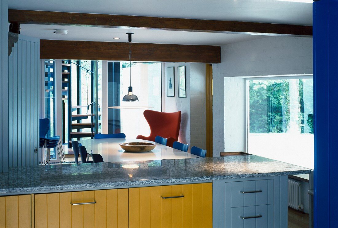 Blick über moderne Küchenzeile mit farbigen Holzfronten und Granit-Arbeitsplatte auf Essplatz mit Fifties-Stühlen