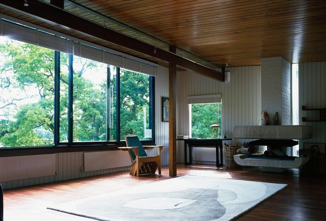 Offener Wohnraum in modernem Holzhaus mit Wand- und Deckenpaneelen, grossen Schiebefenstern und skulpturalem Kamin