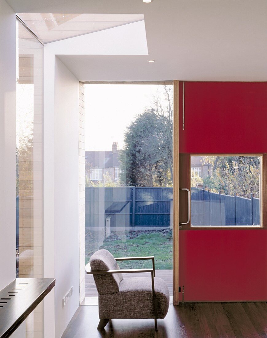 Moderne, rote Eingangstür mit grossen Fensterflächen und Retrosessel
