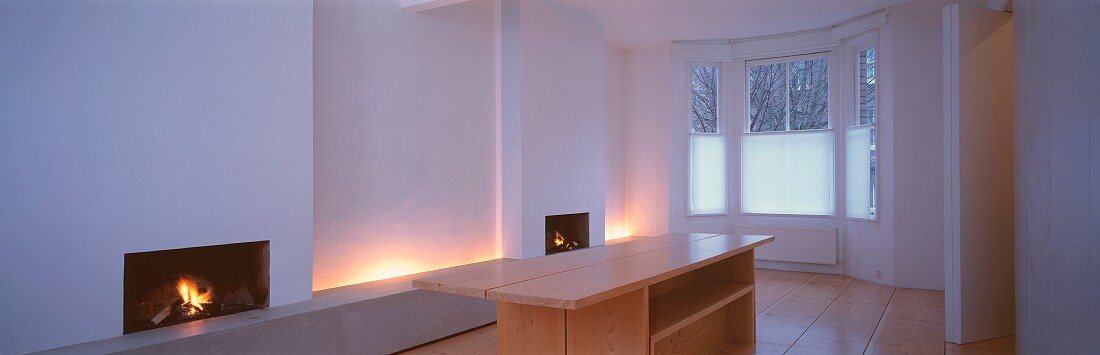 Simple, white living space with bay window and indirect lighting between two open fireplaces