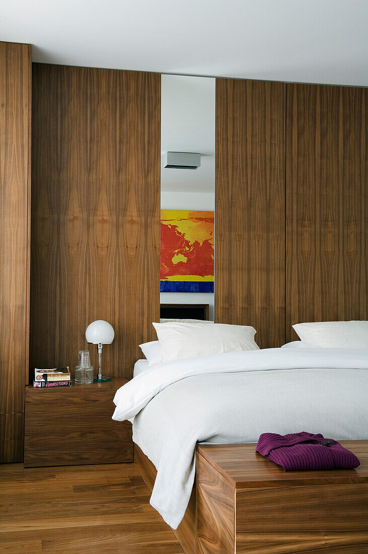Schlafzimmer mit Holzverkleidung und farbigem Wandbild über dem Bett