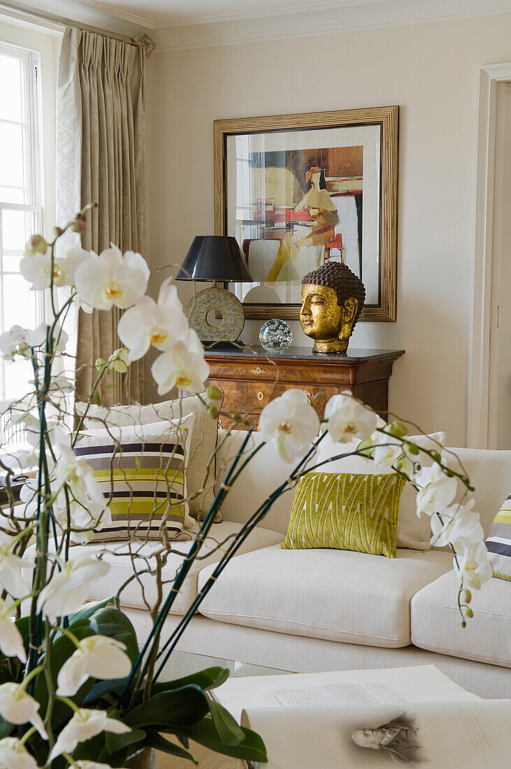 Wohnzimmer mit weißen Orchideen, weißem Sofa und goldener Buddha-Dekoration