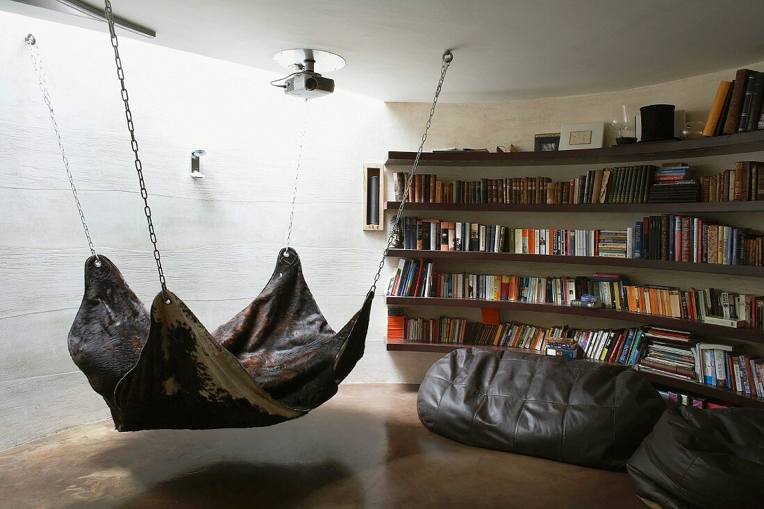 Indirektes Licht von oben in runder Bücherecke mit Hängematte aus Tierfell und Sitzsäcken