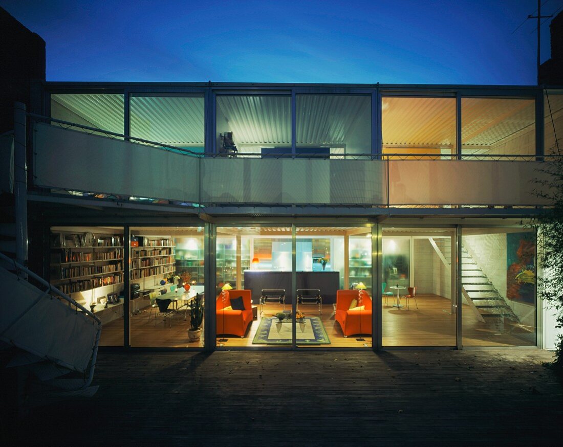 Twilight view of illuminated, contemporary living space with orange sofas and bookcases