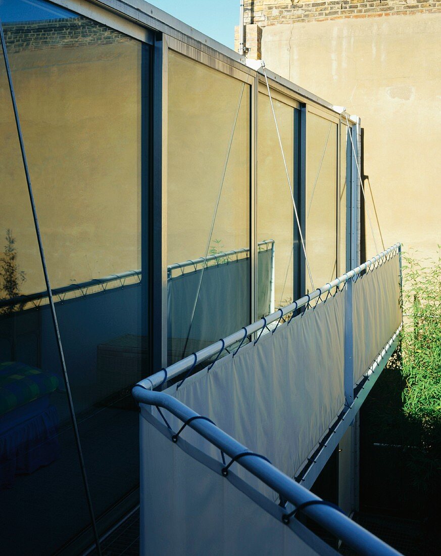 Spiegelung auf Glasfassade eines zeitgenössischen Wohnhauses und vorgesetzte Brüstung mit verspanntem Segeltuch