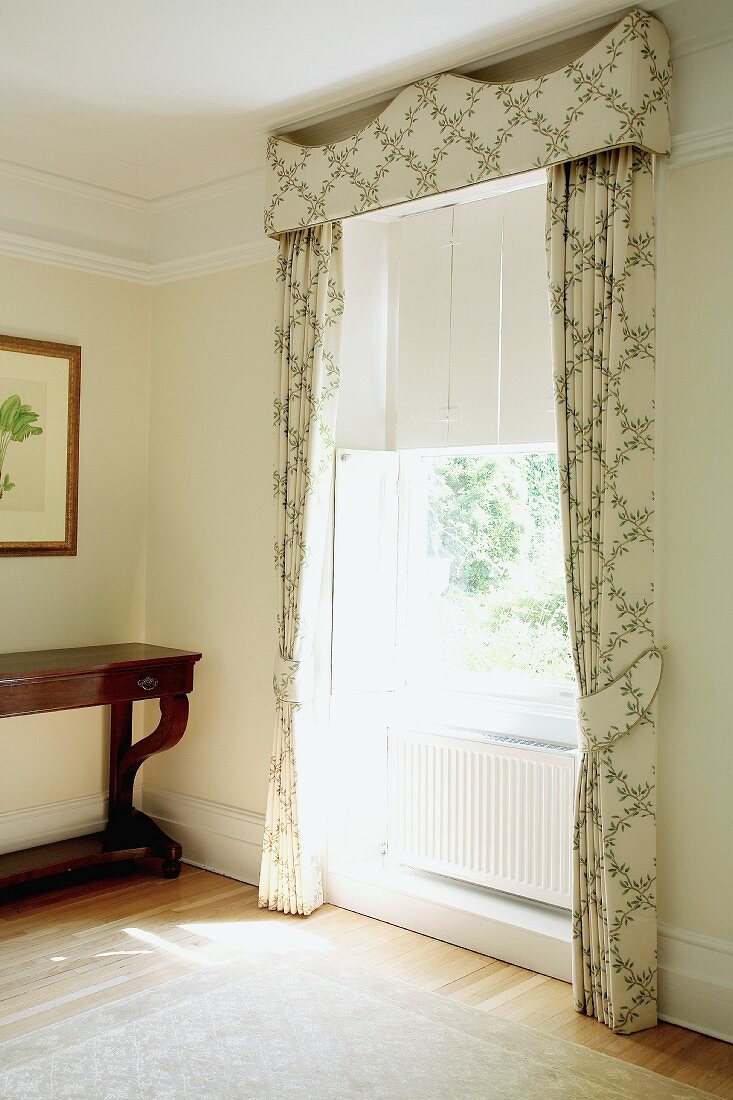Light, patterned curtain with matching pelmet next to antique console table in traditional living room