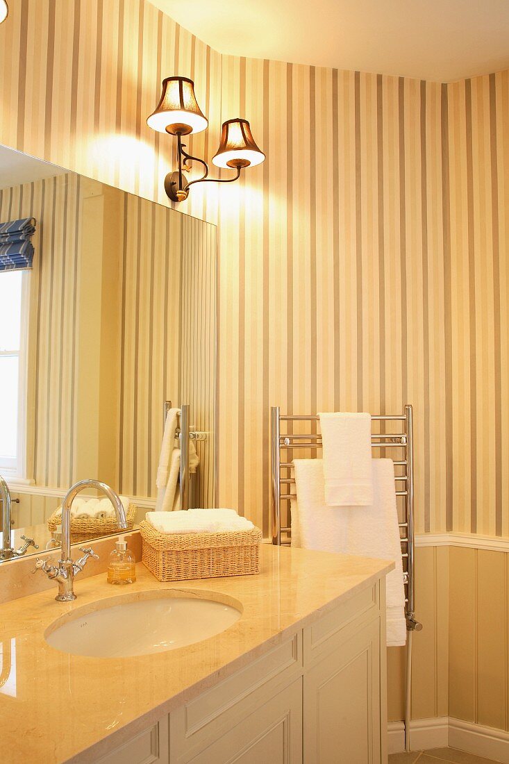 Cremefarbenes Badezimmer im traditionellen Stil mit modernem Handtuchheizkörper vor gestreifter Tapete und brennendem Schirmlämpchen