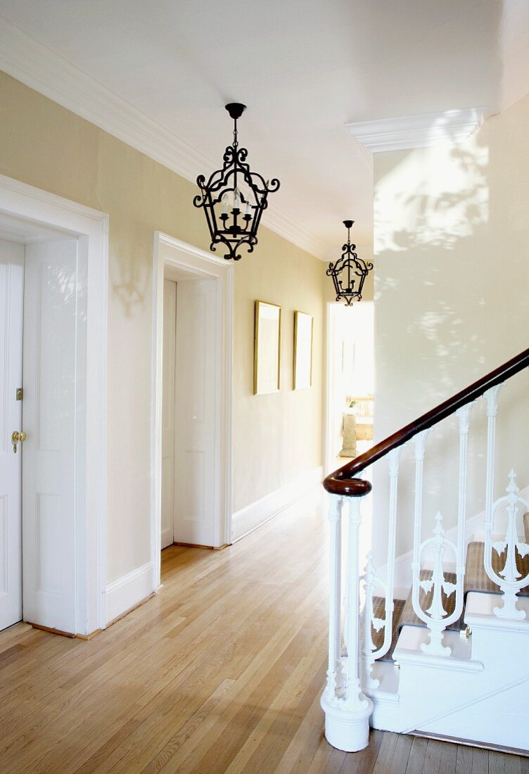 Wrought iron pendant lamps and wooden staircase with antique, carved balustrade in English house