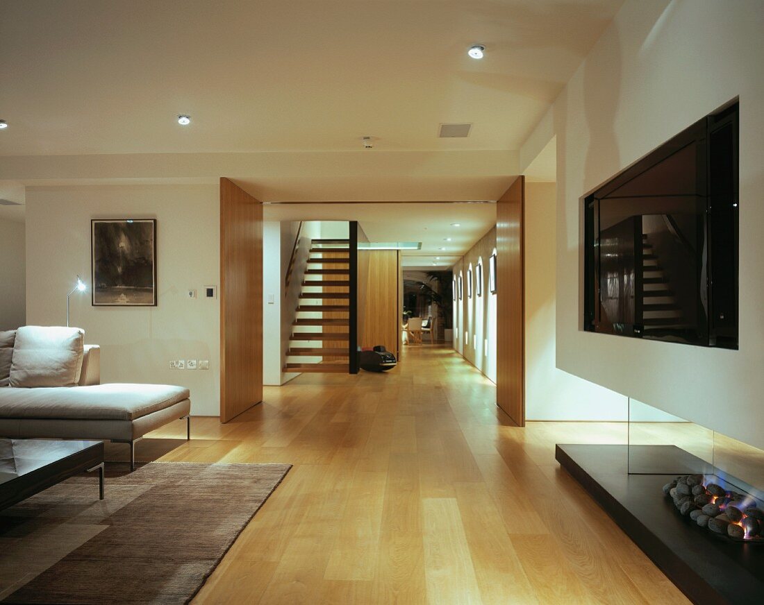 Offenes Wohnzimmer mit modernem Kamin, Blick auf schwebende Holztreppe und Schiebeelemente in Gangflucht