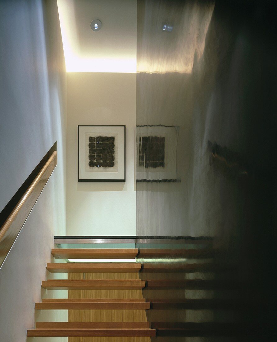 Offene Holzstufen zwischen Zimmerwand mit ebenengleich integriertem Handlauf und glänzend schwarzer Tragwand