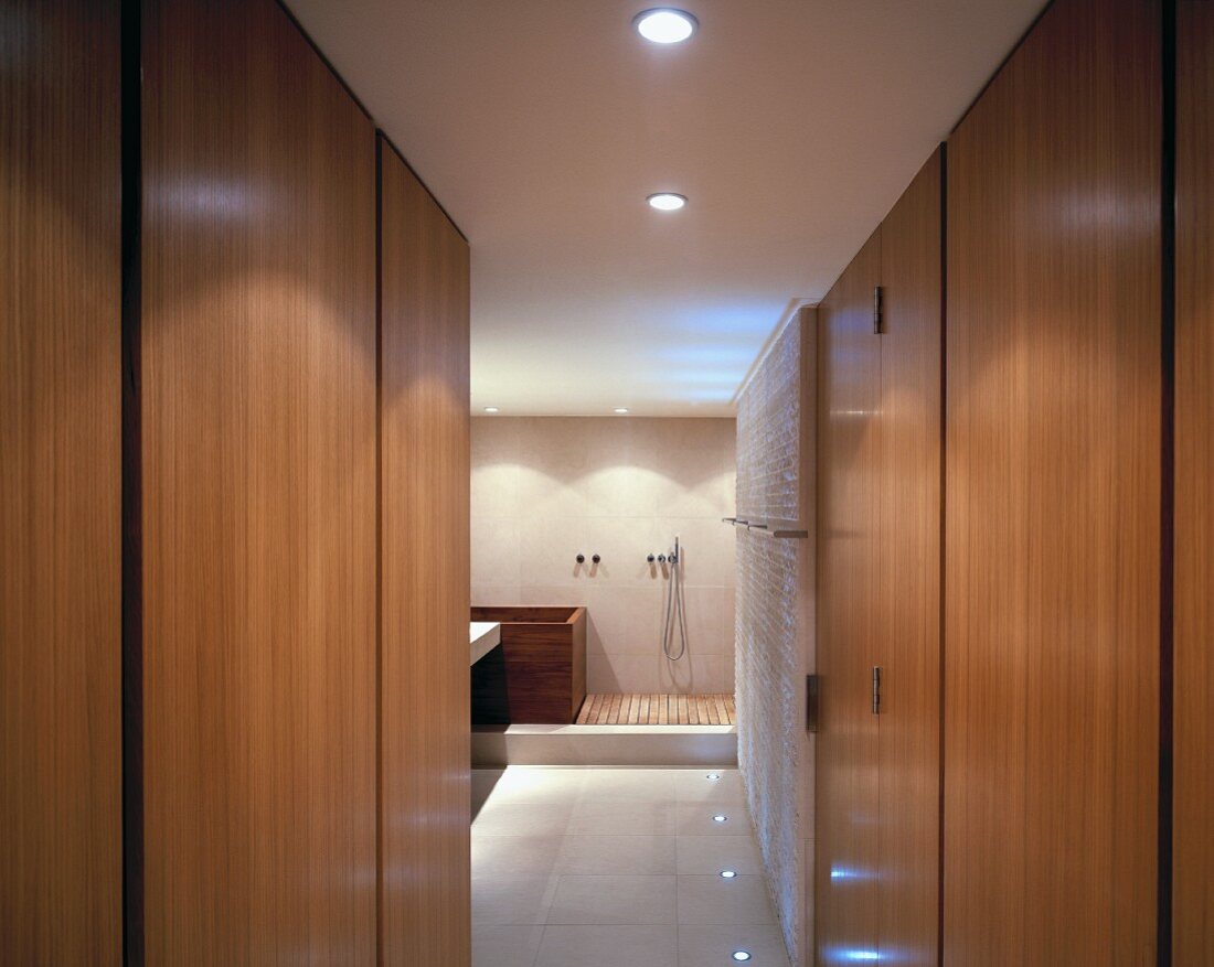 Blick zwischen Schrankwänden auf hölzerne Badewanne und Dusche mit Holzrost im modernen Bad ensuite