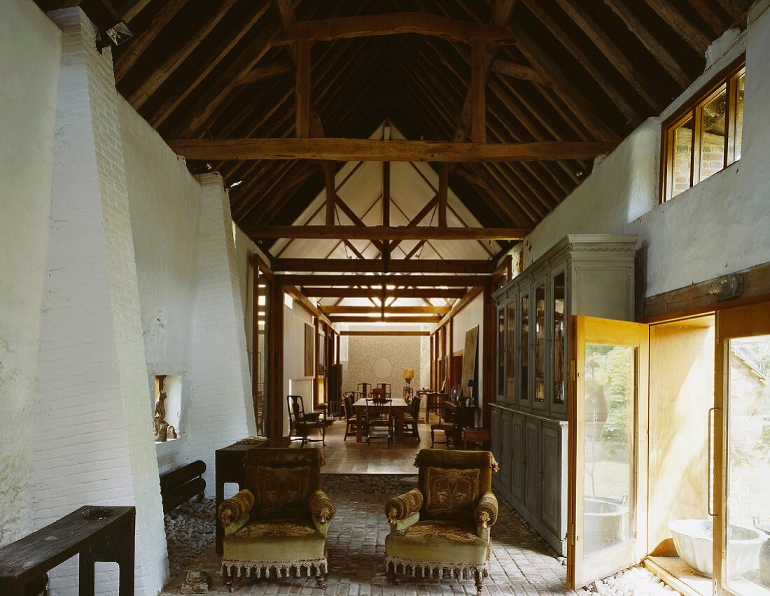 Antike Sessel auf altem Terracottaboden unter historischem Dachstuhl im Kontrast zu moderner, gelber Terrassentür