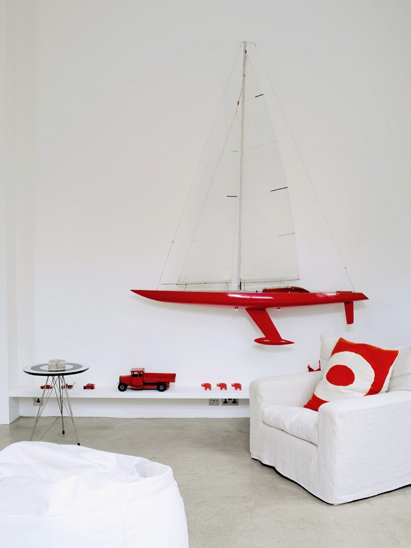 Bright red accessories and model sailing boat on wall combined with white covered chair and beanbag
