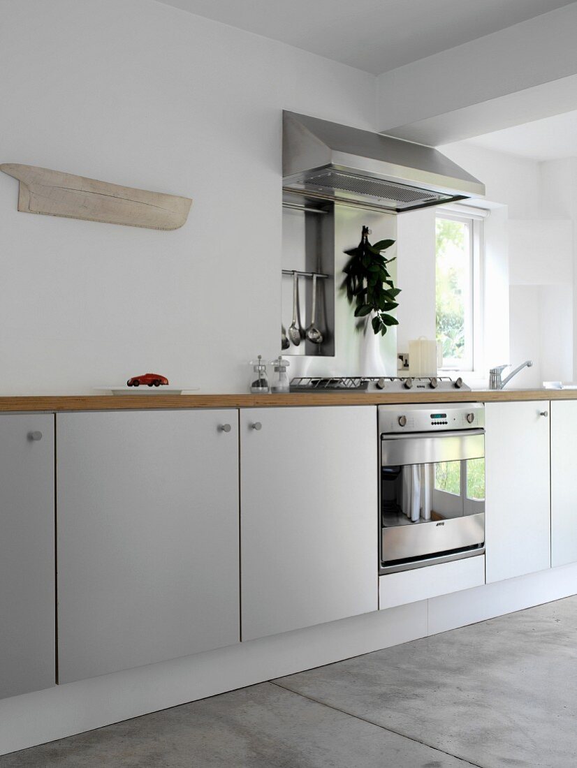 Moderne, weiße Küchenzeile mit Holz-Arbeitsplatte, Edelstahl-Kochelement und Betonboden