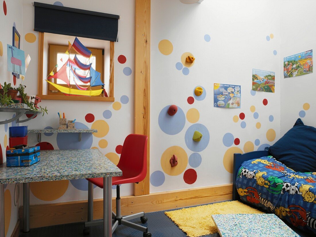 Buntes Kinderzimmer mit Streiflicht von oben auf Farbkreise mit Klettergriffen und Segelboot in Fenster