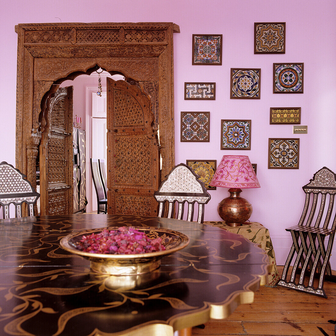 Orientalisch inspirierter Essbereich mit geschnitzter Holztür, Wand in Rosa und Deko