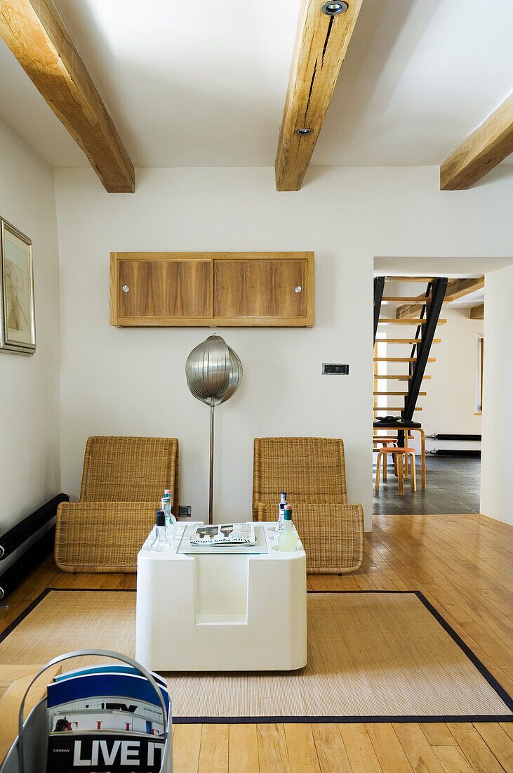 Two rattan armchairs and modern side table in minimalist living room with exposed ceiling beams