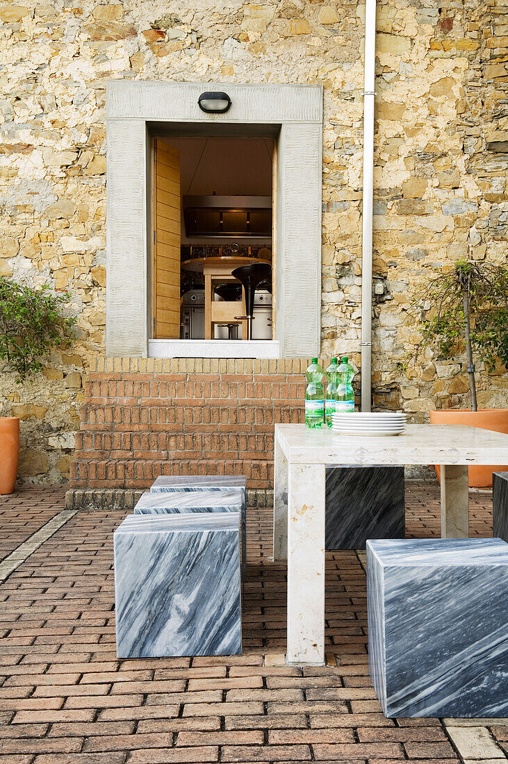 Outdoor seating area with marble table and stools in front of stone wall