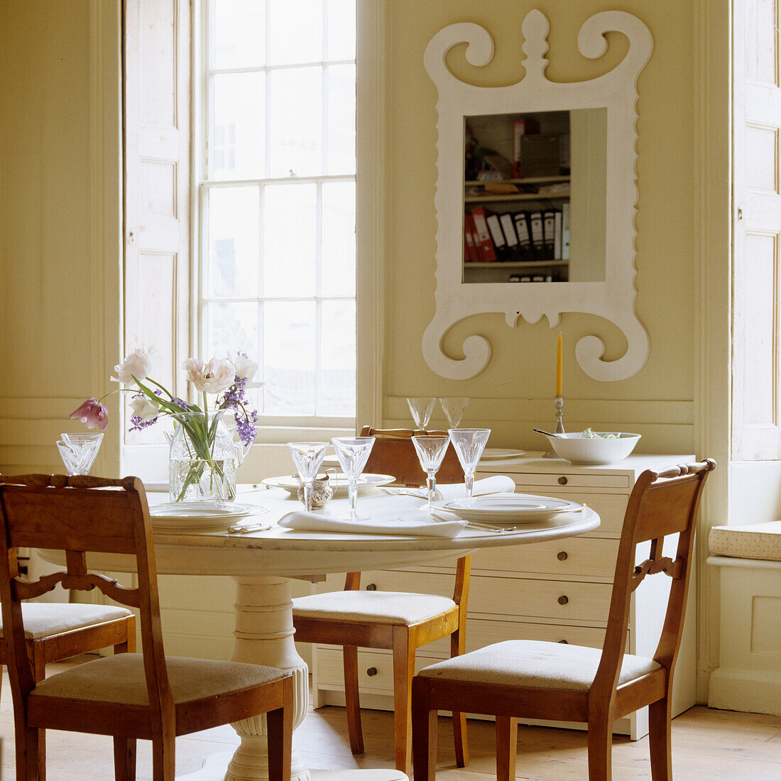 Set dining table with wooden chairs in front of window and ornate mirror