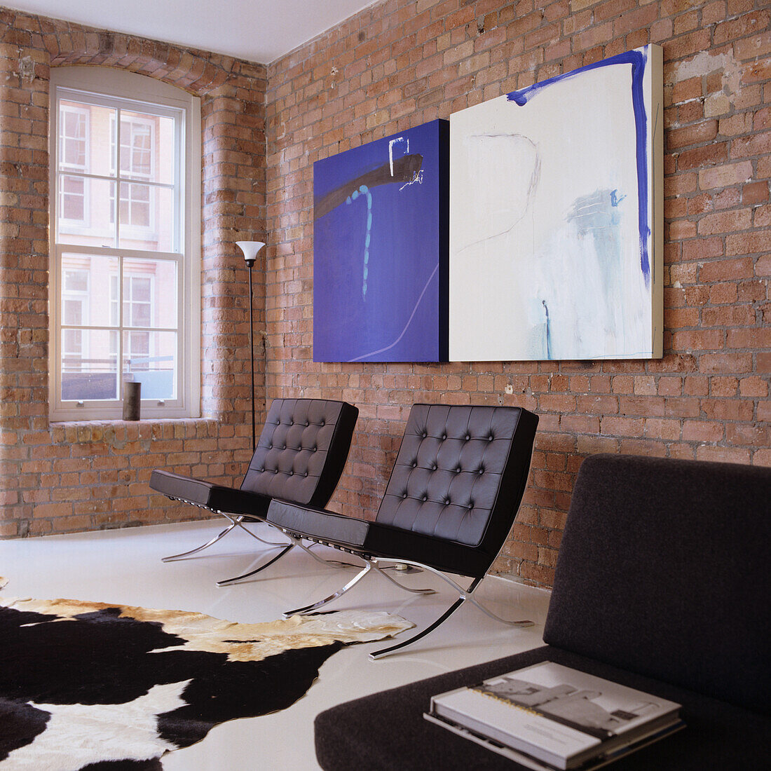 Living room with brick wall, designer chairs and abstract art