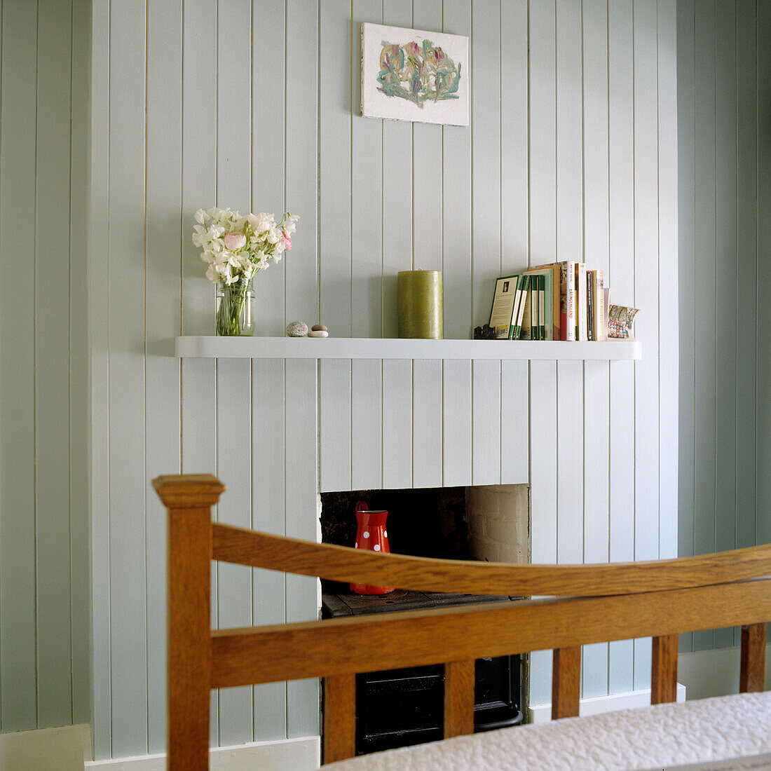 Fireplace with white wood panelling and shelf with decorations and books