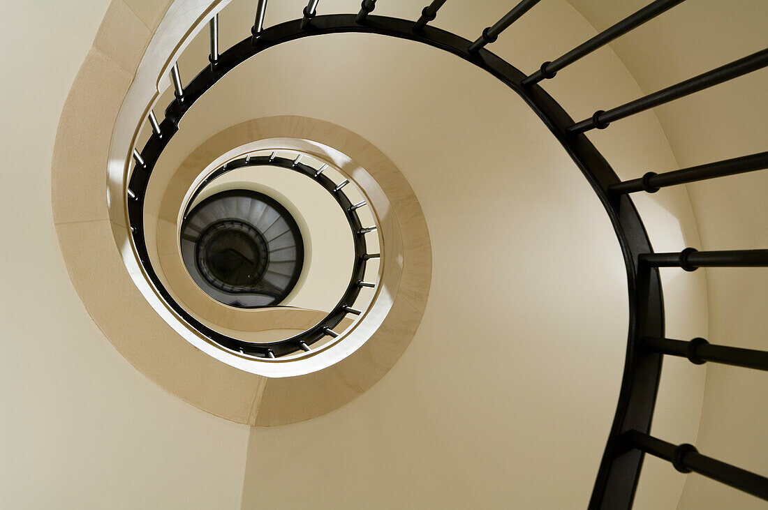 Spiral staircase with dark banisters and light-coloured walls