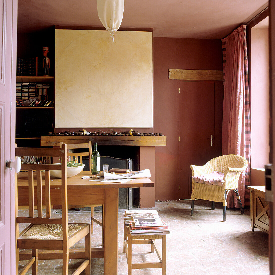 Dining room with wooden table, chairs and wicker armchair, open fireplace and shelves