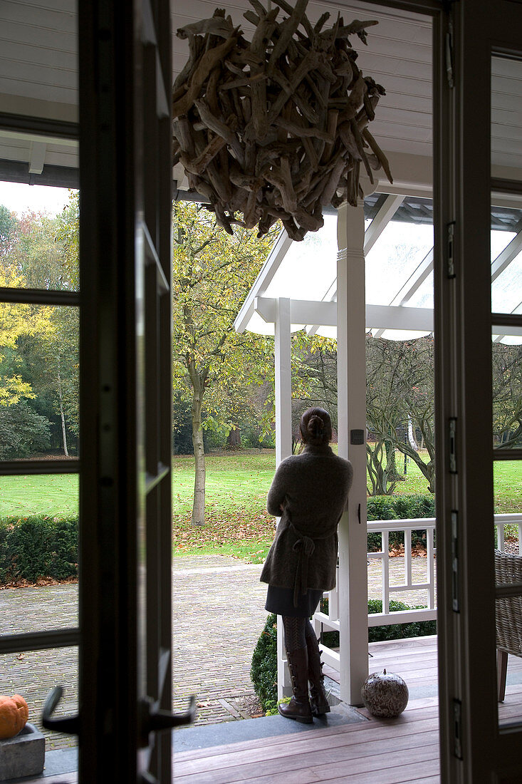 Blick in den Garten mit Herbststimmung - Frau auf Terrasse eines Landhauses