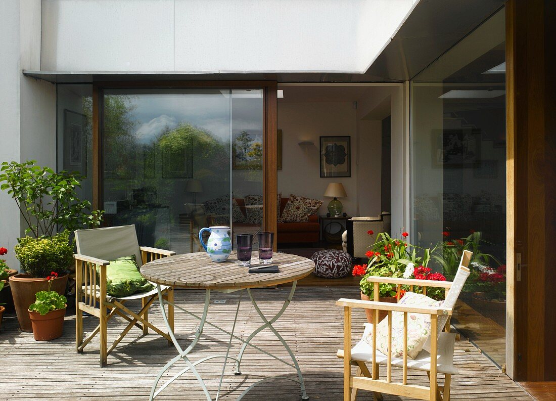 Terrasse mit Holzboden, Tisch & Stühlen vor Glasschiebetüren