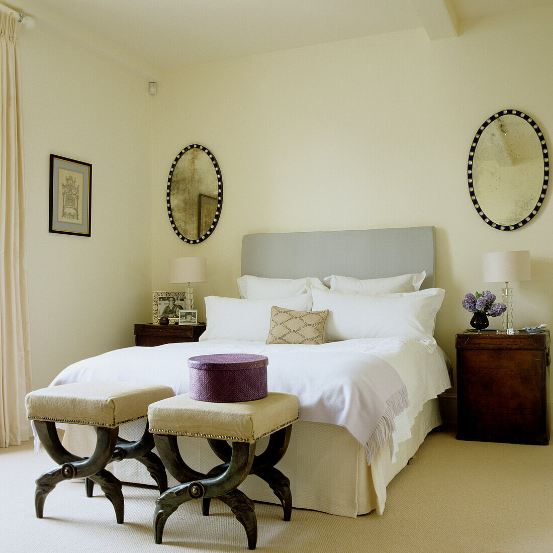 Double bed with grey headboard and upholstered stools in the bedroom