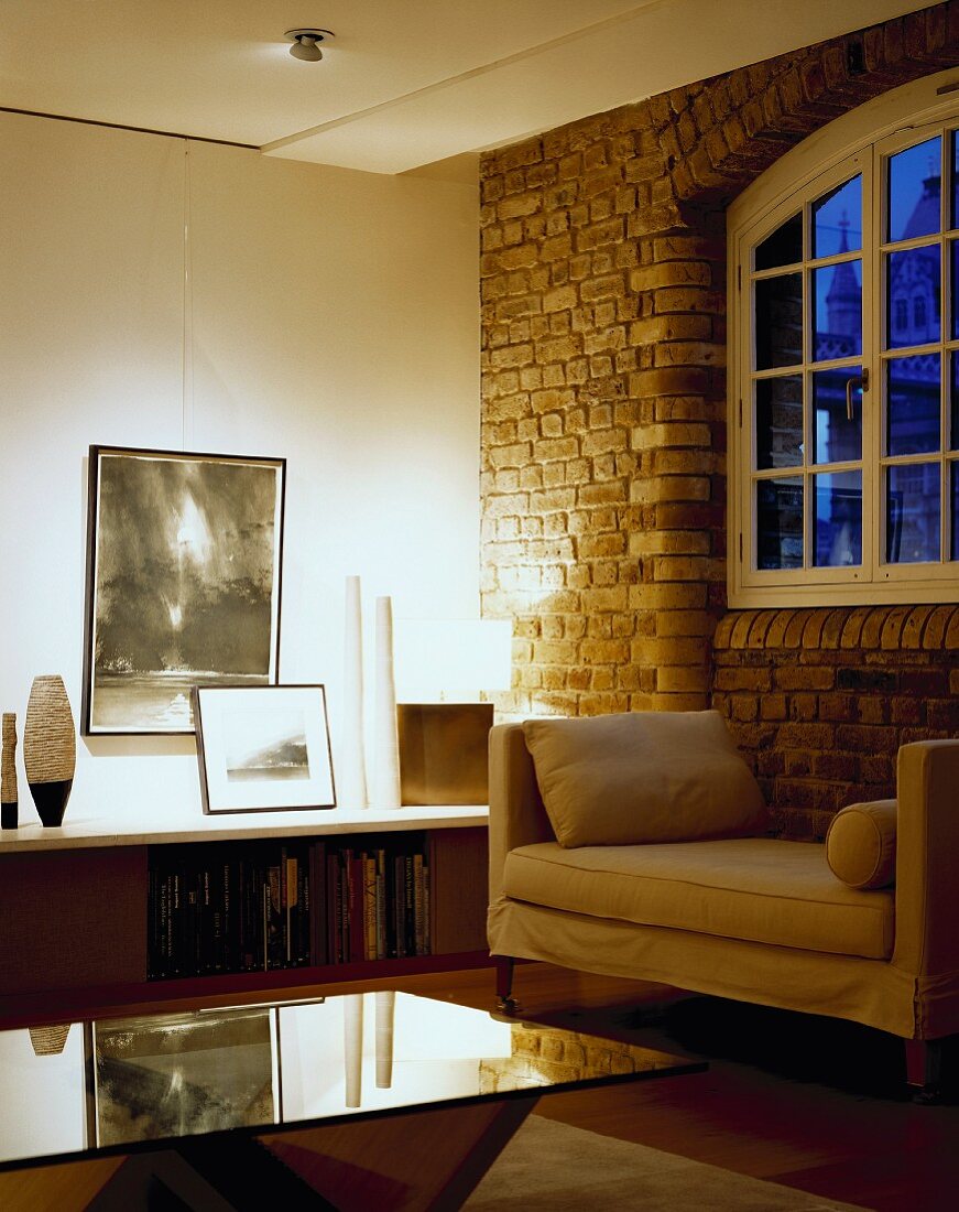 Elegantes Wohnzimmer mit Polsterliege vor der Ziegelwand und Glastisch