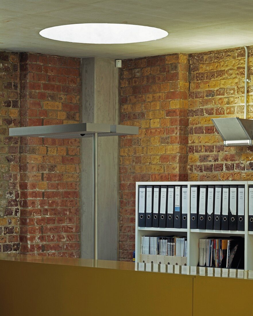 An office with a round skylight, rustic brick walls and a concrete ceiling