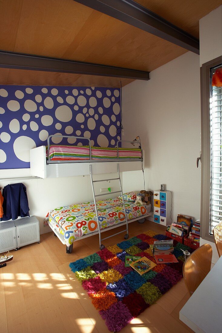 Fröhliches Kinderzimmer unter der Dachschräge mit buntem Teppich im Schachbrettmuster und blauer Tapete mit großen weissen Punkten