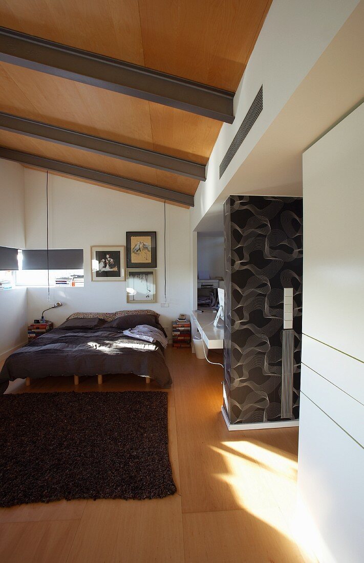Schlafzimmer mit Wandgestaltung im Seventies Stil, großem Doppelbett unter der Dachschräge und Fensterschlitzen