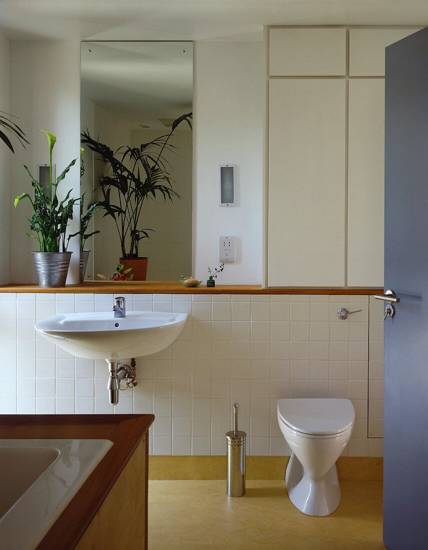 View of modern, white-tiled bathroom through open door