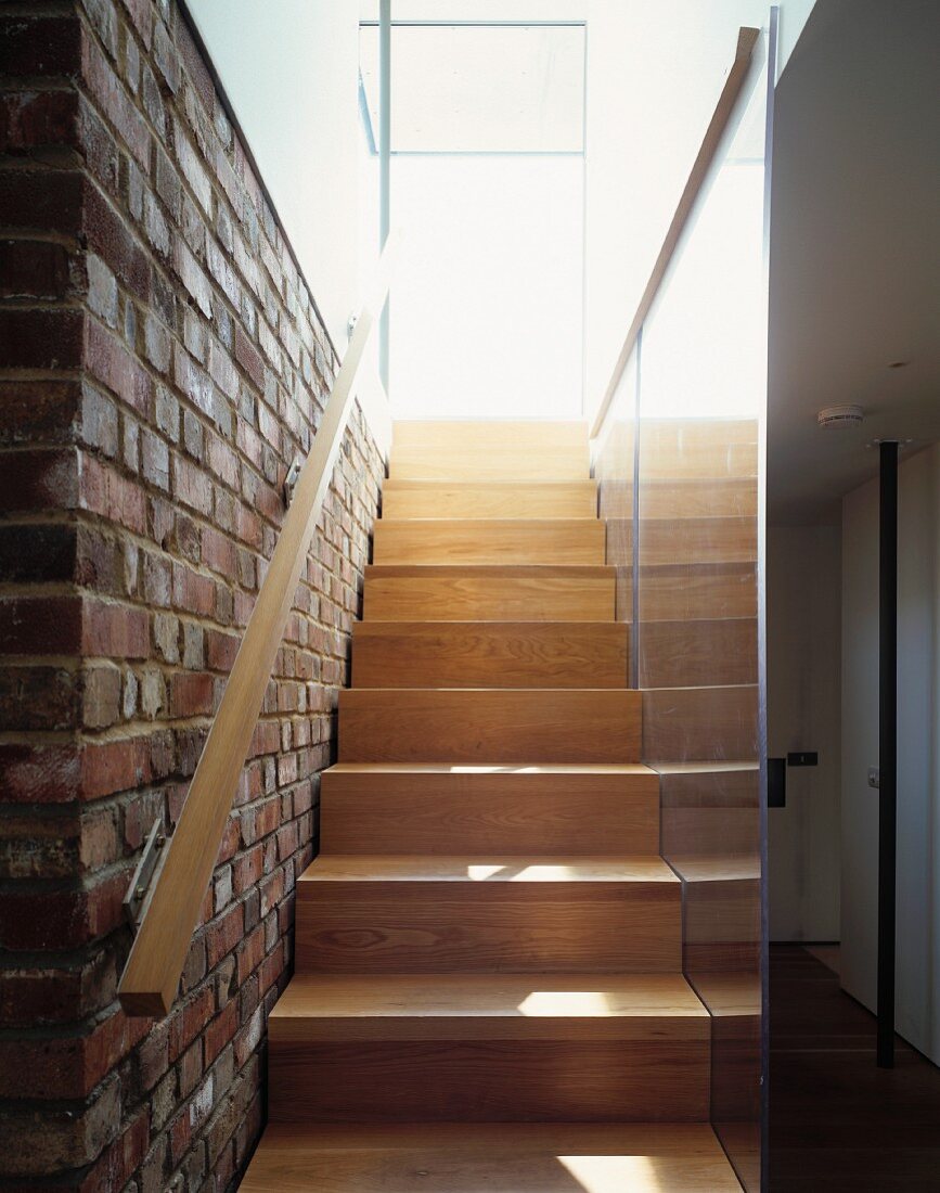 Modern wooden staircase with handrail on brick wall