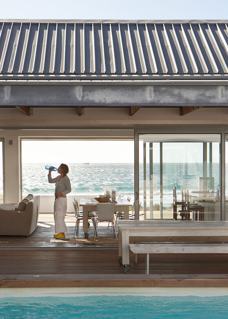 Terrace with pool and dining area by the sea, person drinking water