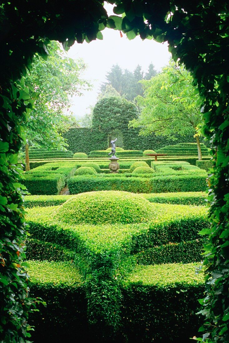 Blick durch Öffnung in Hecke auf Gartenanlage mit in Form geschnittenen Hecken, ein Beispiel für Gartenarchitektur.