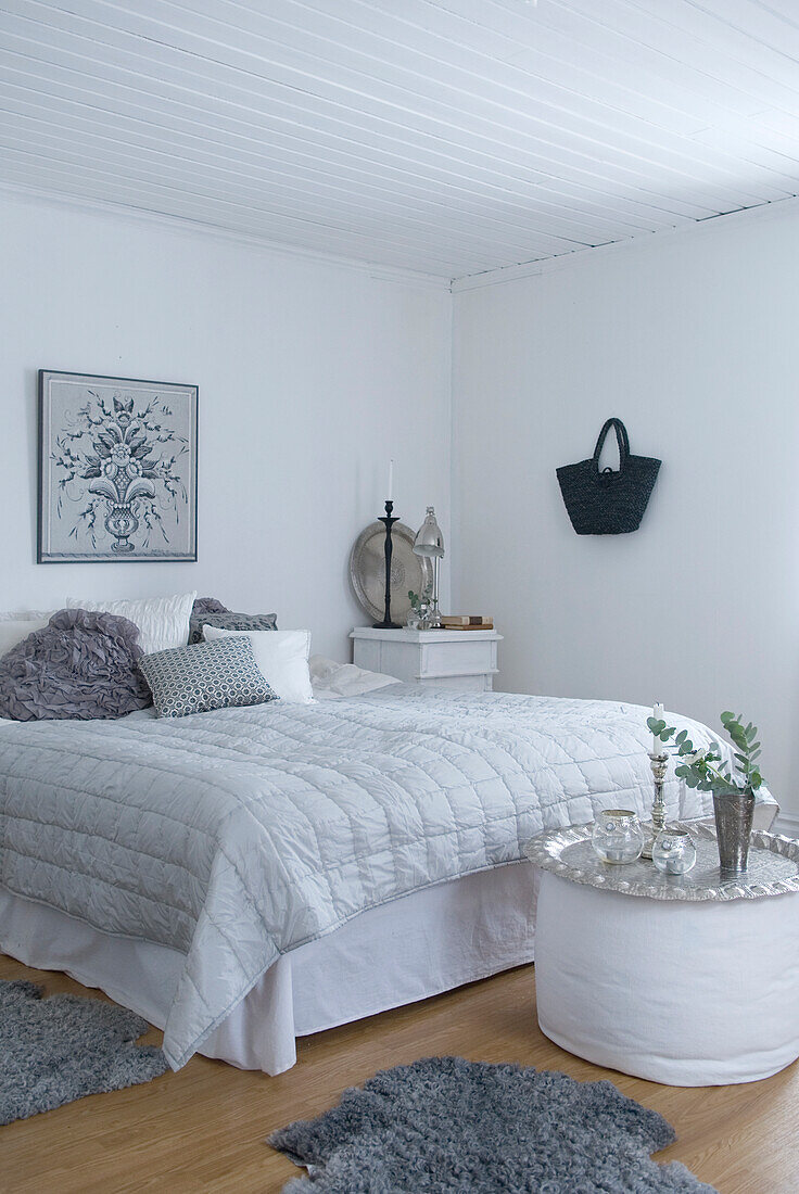 Schlafzimmer in Weiß mit Bild über Bett, Nachttisch und Felle in Grautönen auf dem Boden