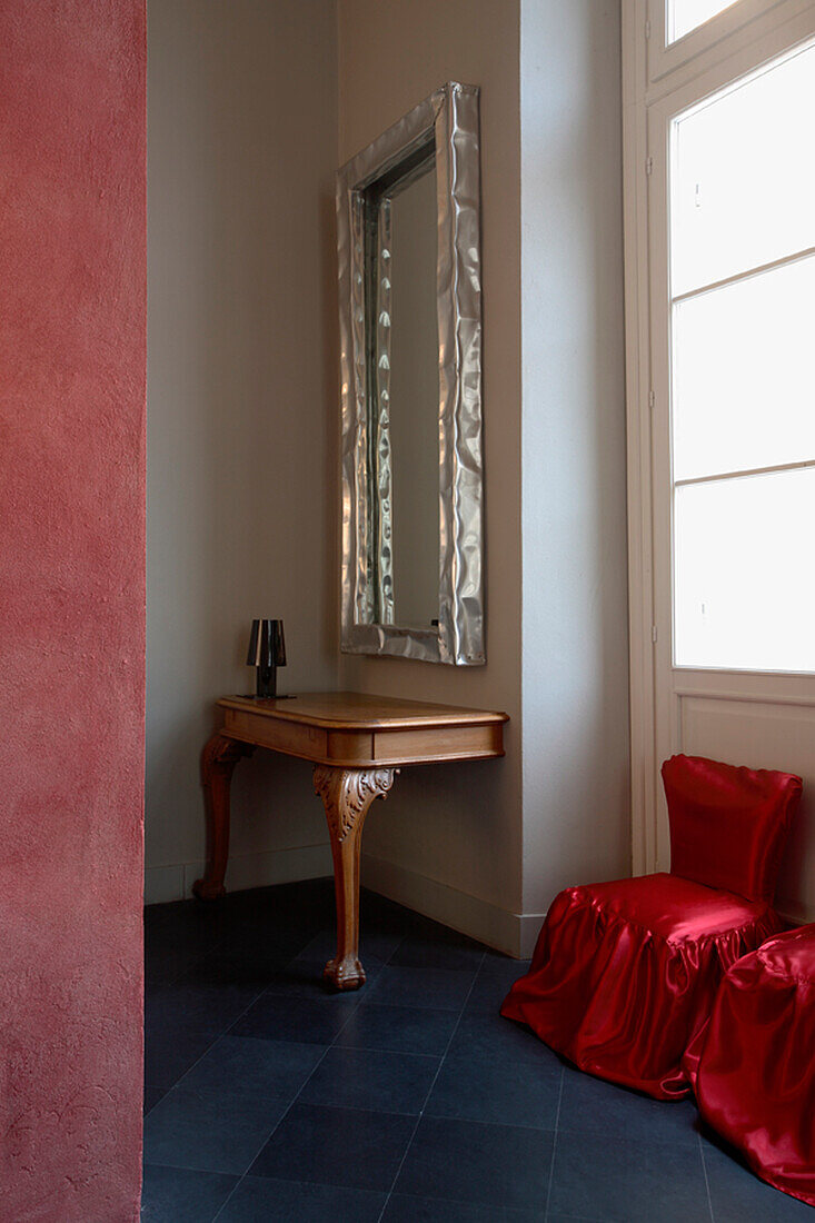 Console table with mirror, dark blue floor tiles and chairs with red fabric covers