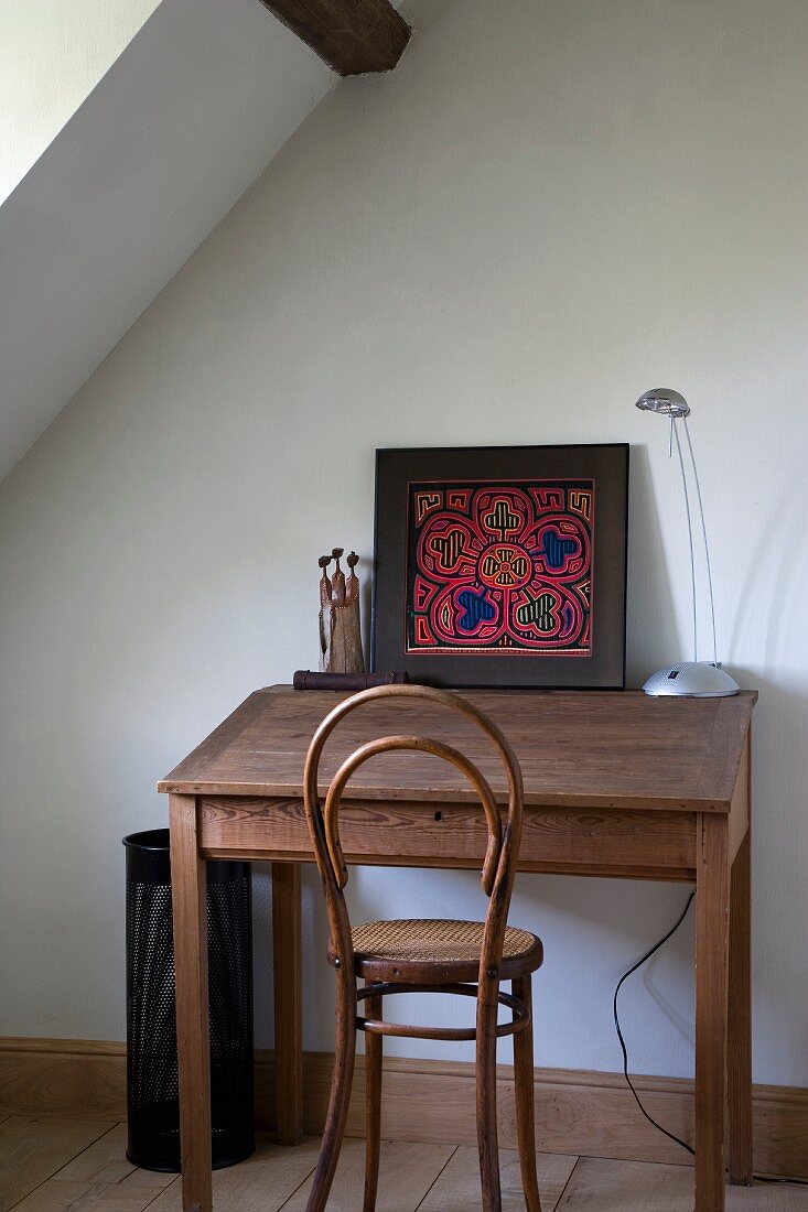 Colourful artwork on simple wooden desk with antique Thonet chair