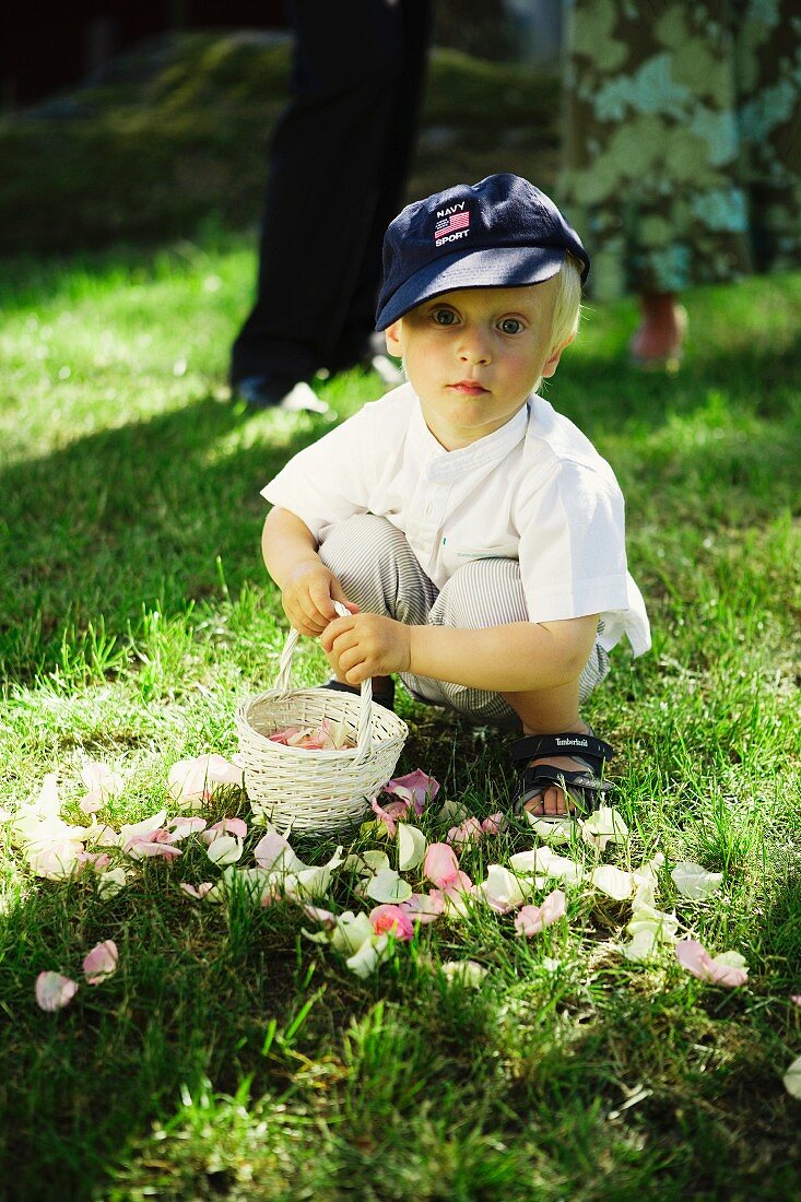 Kleiner Junge mit Korb und Rosenblütenblättern im Garten