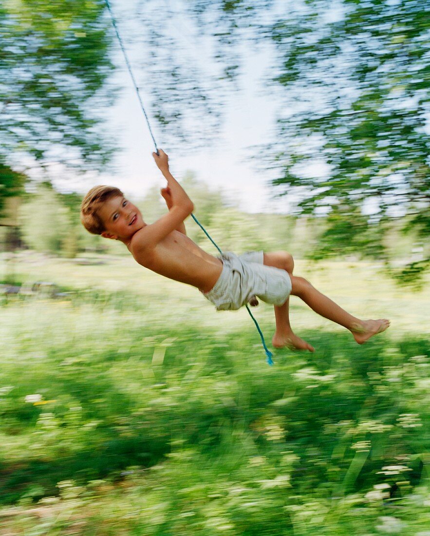 Boy swinging on rope in garden