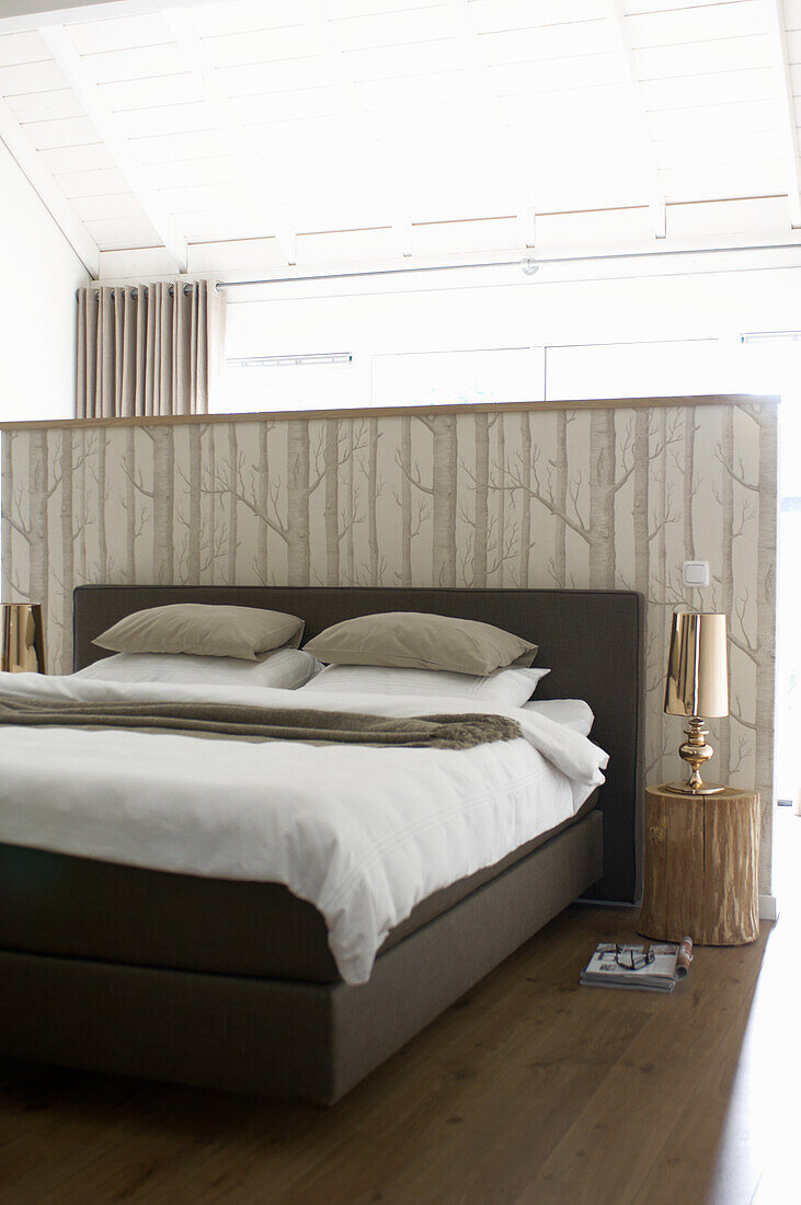 Bed in front of room divider with birch forest motif in light-coloured bedroom