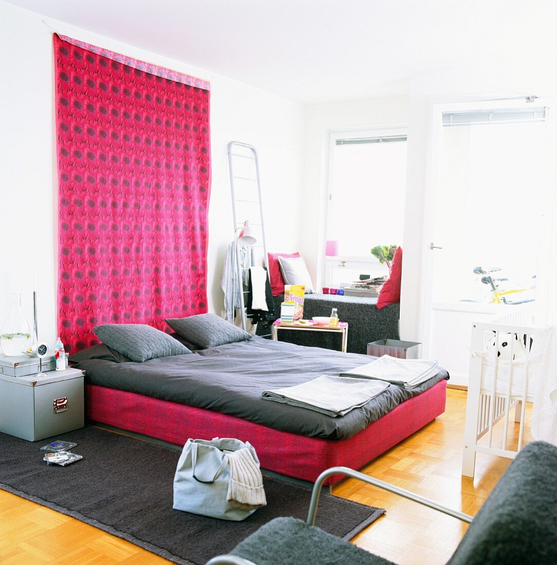 Schlafzimmer mit pinkfarbenem Wandteppich und grauer Bettwäsche