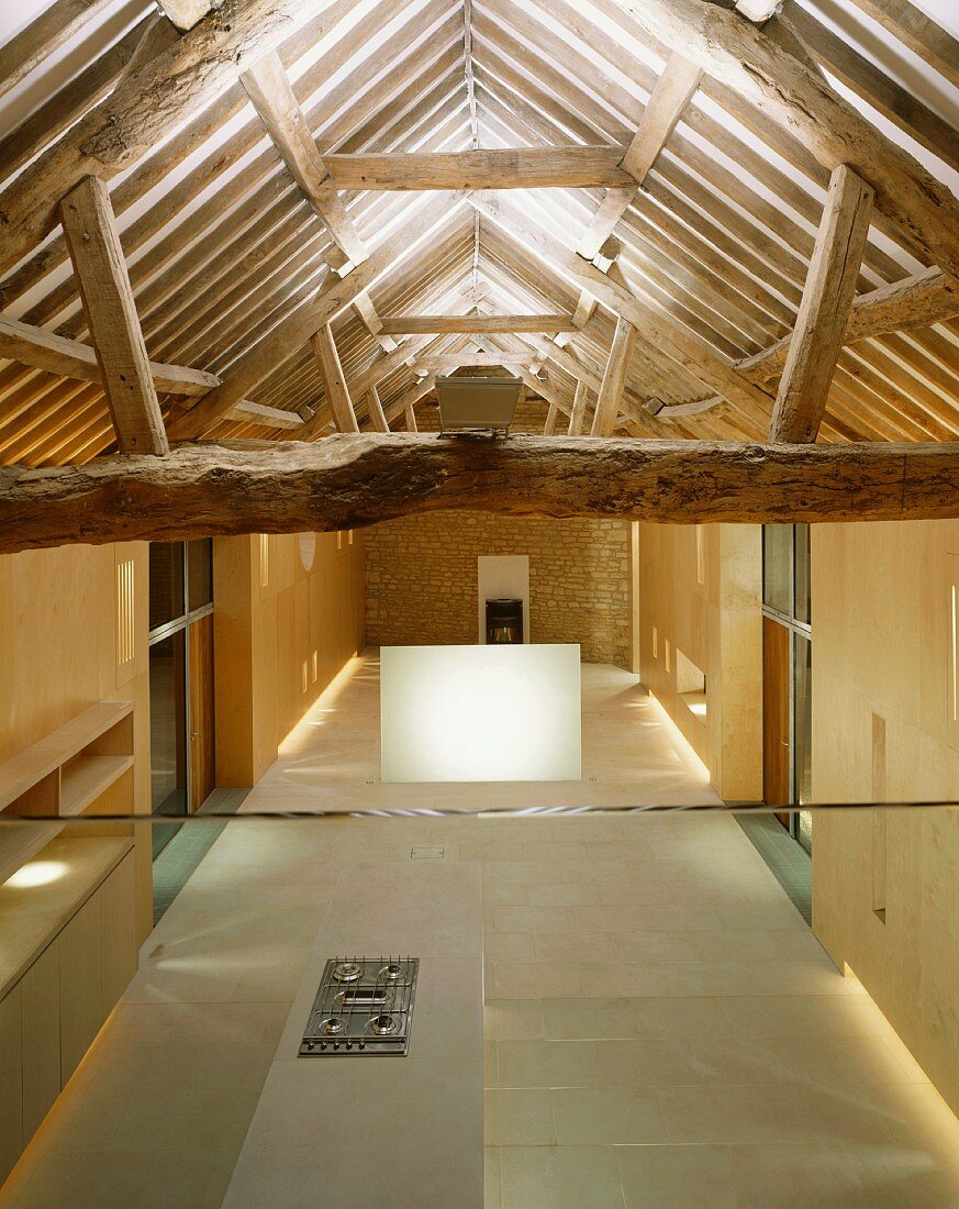 Designer-style, open-plan room in converted house with view of rustic roof timbers and open-plan kitchen below