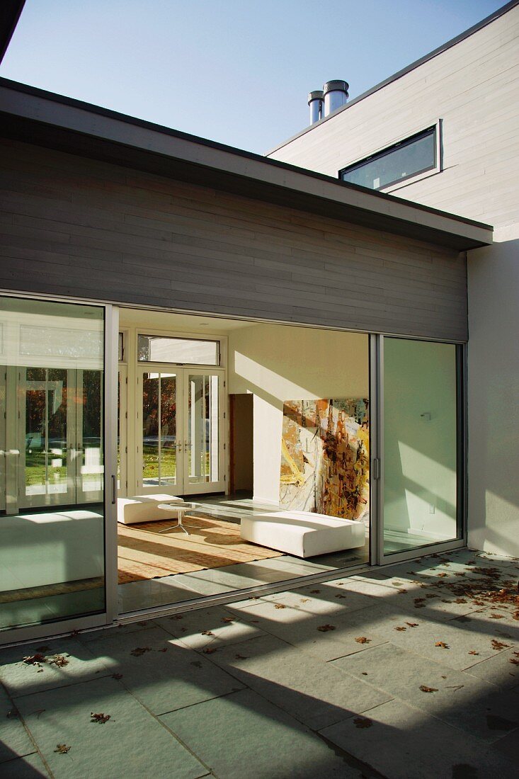 Innenhof in Herbststimmung und Blick durch offene Glasschiebetüren in Wohnraum
