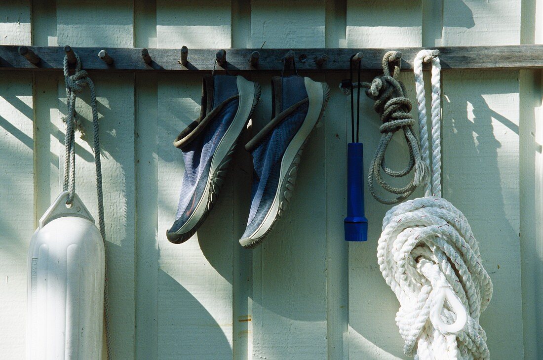 Eine Boje, ein Paar Schuh und Seil hängen an Haken am Hauswand