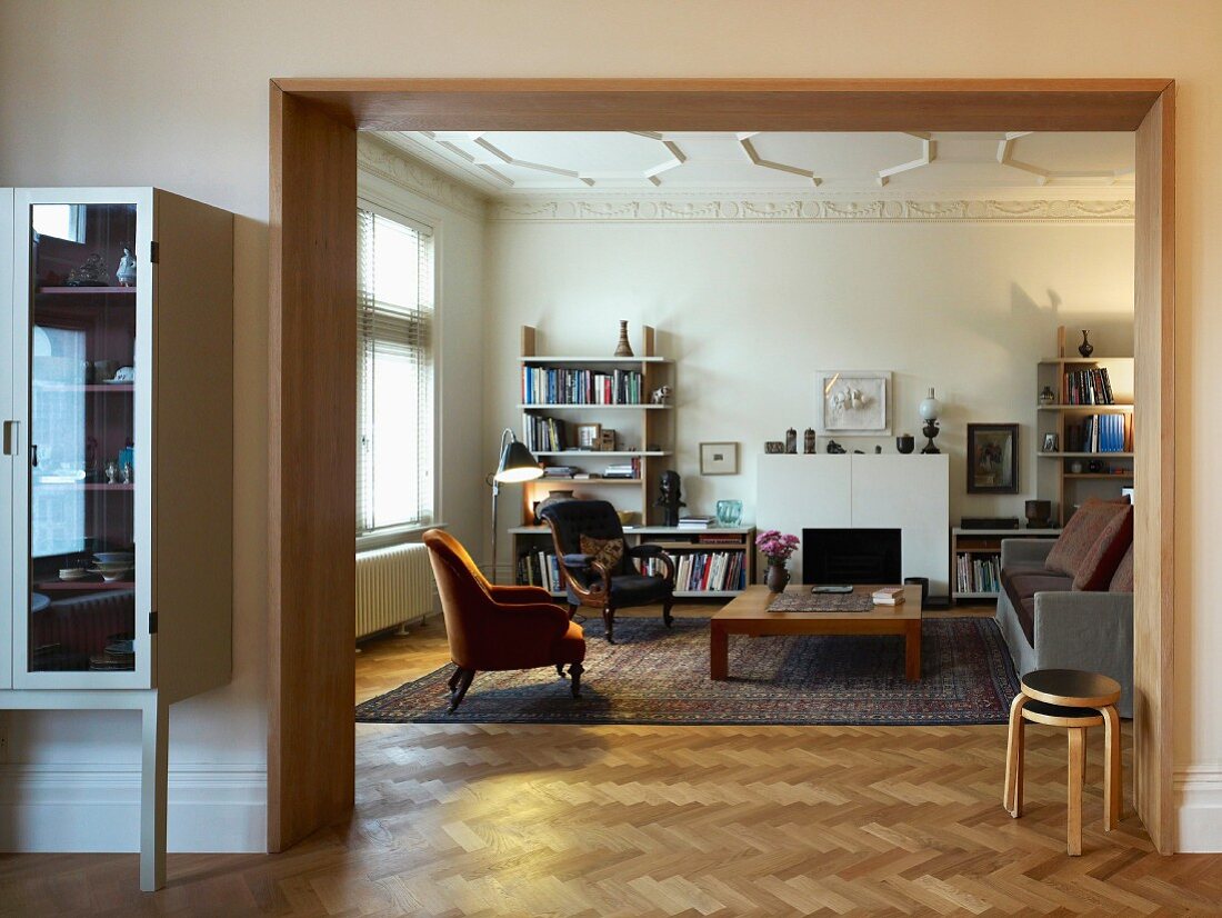 View through wide doorway into modern living room with antique armchairs