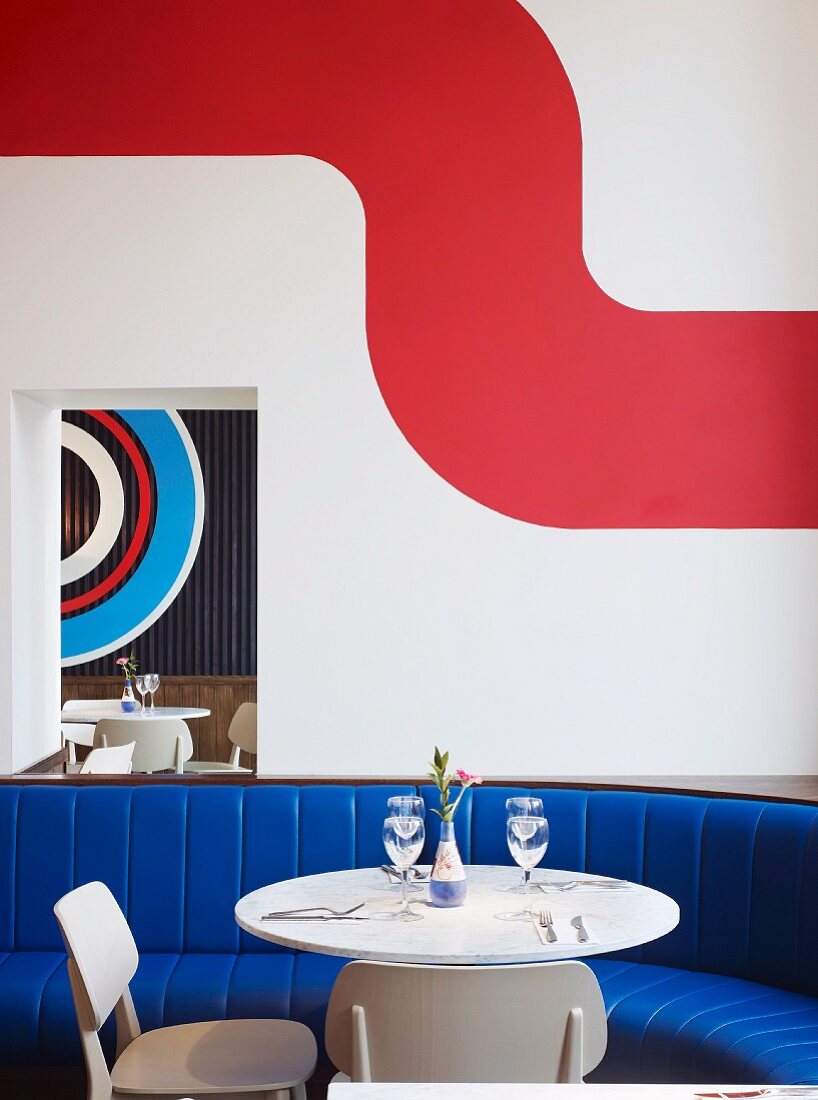 Tisch mit Stühlen und Sitzbank mit blauem Polsterbezug vor Wand mit moderner Farbgestaltung